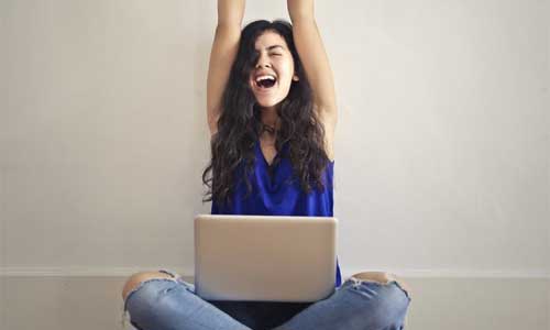 ノートパソコン膝に置き両手を挙げて喜ぶ胡坐の姿勢の女性
